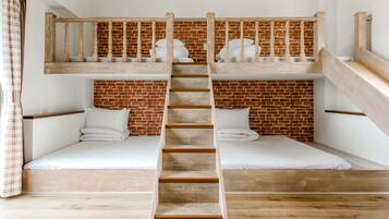 A bunk bed room with a wooden ladder, white bedding, and a brick wall.