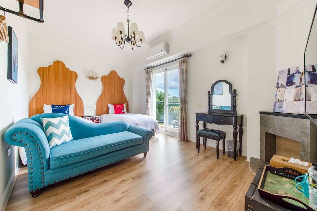A bedroom with a large bed, a blue sofa, a desk, and a fireplace.