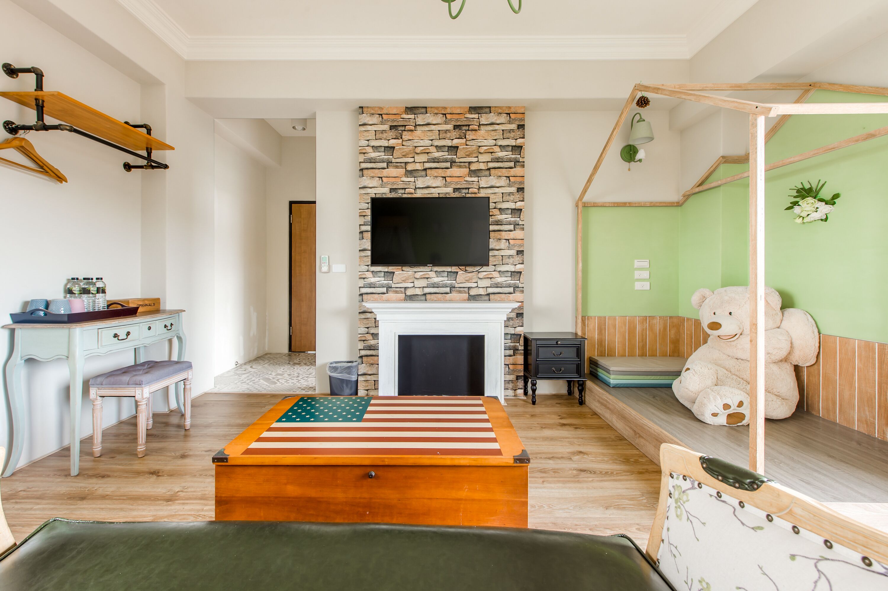 A living room with a stone fireplace, a television mounted above it, a wooden bench, and a large teddy bear.
