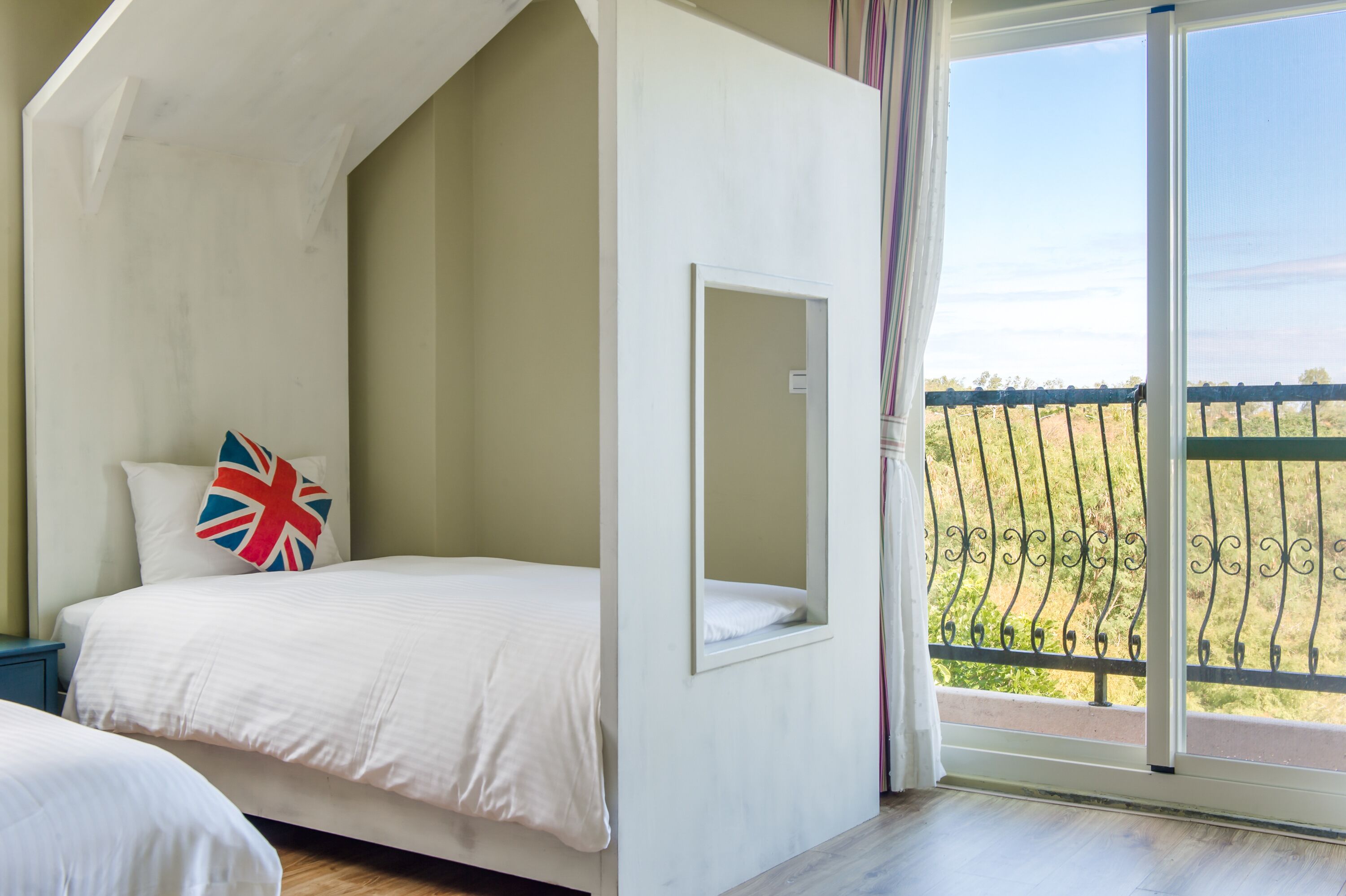 A bedroom with a bed, a small window, and a balcony with a railing.
