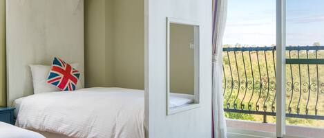 A bedroom with a bed, a small window, and a balcony with a railing.