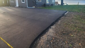 Een oprit naar een huis met garage, een boot afgemeerd aan het water en een gazon met bomen.