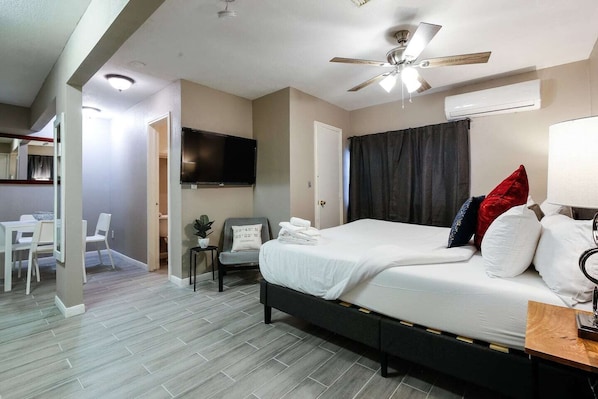 Habitación de hotel con cama, escritorio, silla, televisión, ventilador de techo y aire acondicionado.