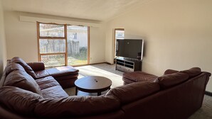 A living room with a large L-shaped sectional sofa, a small round coffee table, a flat-screen TV, and a sliding glass door leading to a backyard. - Spacious three bedroom home located 5 minutes from WEC  (Wilmington)