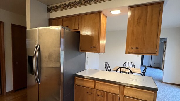 A kitchen with wooden cabinets, a stainless steel refrigerator, and a dining area with a table and chairs. - Spacious three bedroom home located 5 minutes from WEC  (Wilmington)
