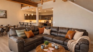 A modern living room with a sectional sofa, a coffee table, and a dining area in the background. - Big Family Lake Retreat | 6BR Table Rock (Cape Fair)