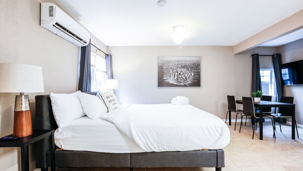 Moderni hotellihuone, jossa on suuri sänky, työpöytä ja tuoli. Seinällä on ilmastointilaite, yöpöydällä lamppu ja seinällä kehystetty taulu.