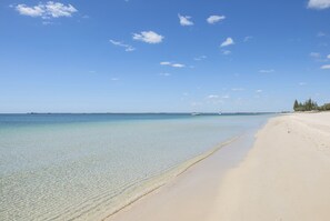 Una playa con agua cristalina, un muelle a lo lejos y una orilla arenosa.