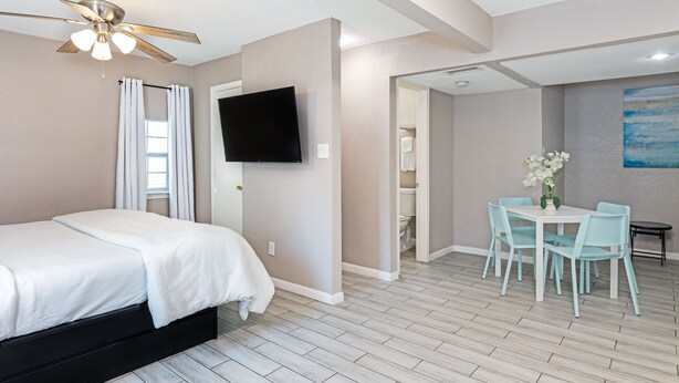 Une chambre d’hôtel comprenant un lit, un ventilateur de plafond, un téléviseur à écran plat, un coin repas avec une table et des chaises, et un tableau au mur.