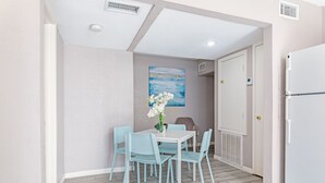 Un petit coin repas avec une table blanche et quatre chaises bleu clair, un vase avec des fleurs blanches et un tableau bleu accroché au mur.