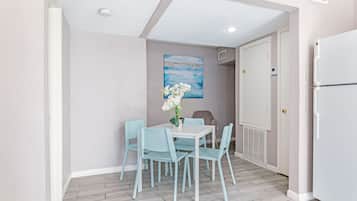 Un rincón comedor compacto con una mesa blanca y cuatro sillas azul claro, un florero con flores blancas y un cuadro azul en la pared.