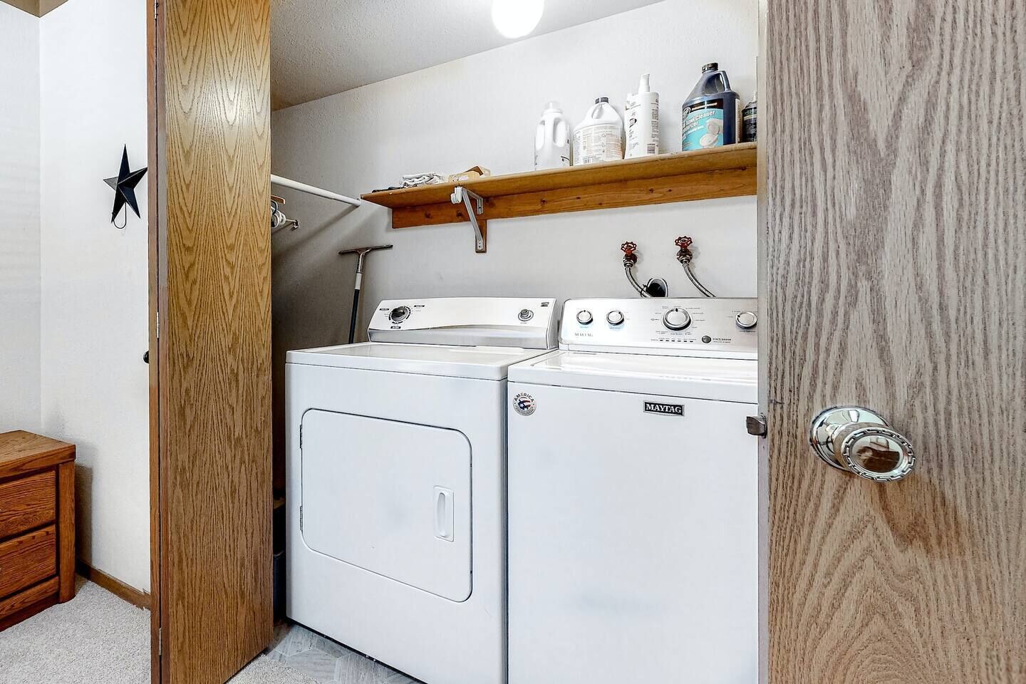 A laundry room with a washing machine and dryer, wooden shelves with cleaning supplies, and a star decoration on the wall.