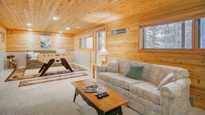 A log cabin interior with a wooden ceiling, a sofa, a coffee table, a ski rack, and a sign indicating 'Calamity Jane'.