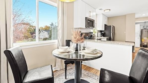 A modern kitchen with white cabinets, a central island, and a dining area with two chairs and a table. - Charming New Unit in the Heart of Roseville (Roseville)