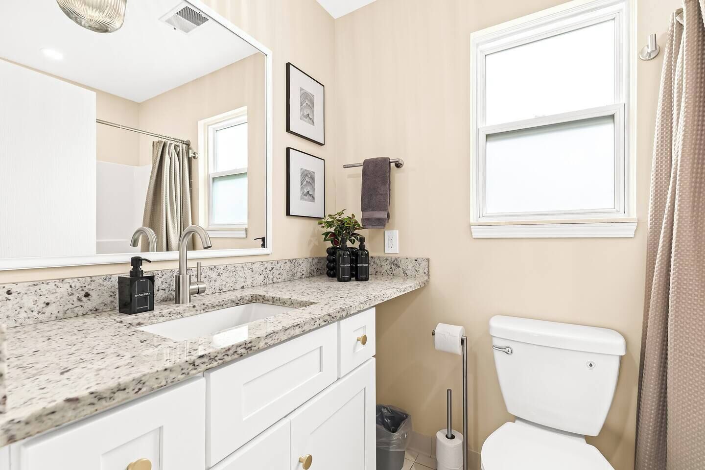 A modern bathroom with a granite countertop, white fixtures, a toilet, and a shower curtain.