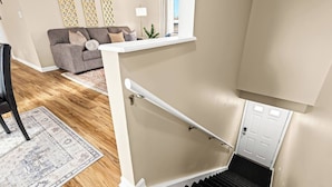 A staircase with a handrail, a wooden floor, a grey sofa, and a patterned rug in a living room. - Charming New Unit in the Heart of Roseville (Roseville)