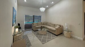 Ein geräumiges Wohnzimmer mit einem beigefarbenen Ecksofa, einem Glastisch und einer Kristallleuchtre.