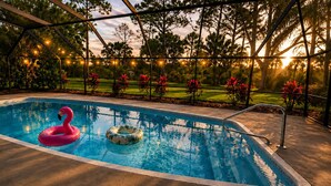 Ein Swimmingpool mit einem Flamingo-Schwimmpfad und einem Palmblatt-Schwimmpfad, umgeben von einer Holzterrasse und Lichterketten.