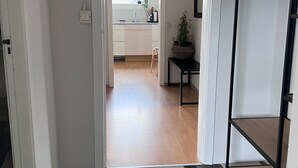 En gang der fører til et køkken med et ternet gulv, en lille skammel og en potteplante.