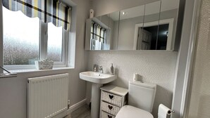 A compact bathroom with a white sink, toilet, and a window with striped curtains. - Spacious House To Accommodate 6 (Shavington)