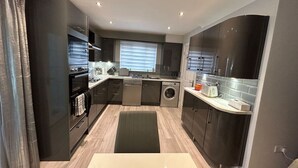 A modern kitchen with dark cabinetry, stainless steel appliances, and a central island. - Spacious House To Accommodate 6 (Shavington)