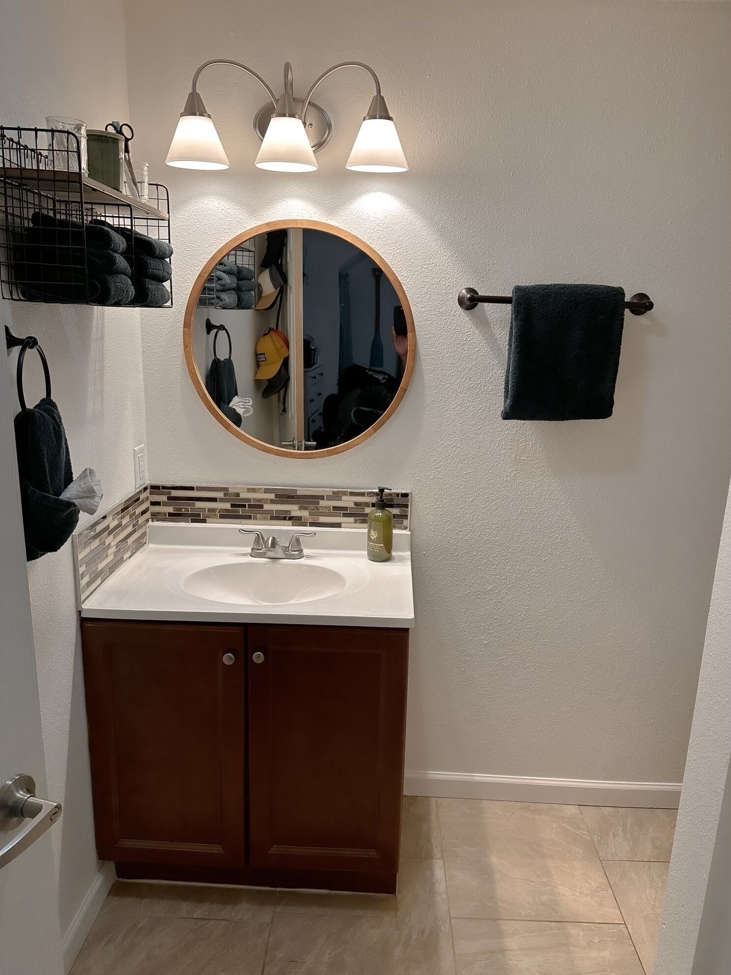Une salle de bain avec un miroir rond, un lavabo et un porte-serviettes.