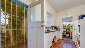 A kitchen with white cabinets, a wooden floor, and a window overlooking a garden.