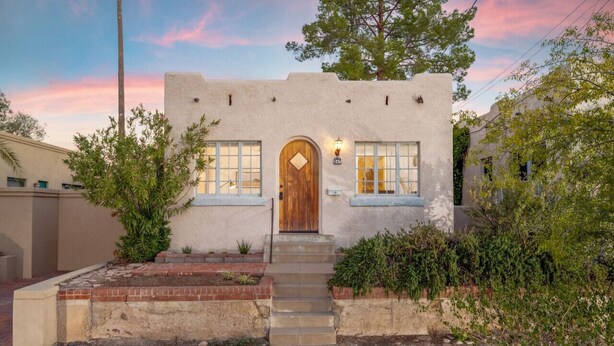 A stucco building with a wooden door, a small set of steps, and a light fixture above the door.