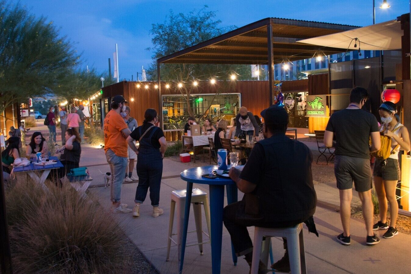 An outdoor dining area with tables and chairs, surrounded by a wooden structure with string lights.
