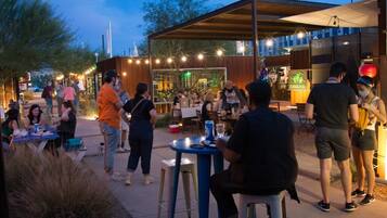An outdoor dining area with tables and chairs, surrounded by a wooden structure with string lights.