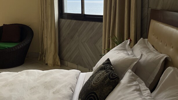 Ein Schlafzimmer mit Bett, Sessel und Meerblick durch ein Fenster.