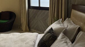 Ein Schlafzimmer mit Bett, Sessel und Meerblick durch ein Fenster.