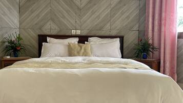 Una cama impecable con sábanas blancas y una manta color beige, flanqueada por dos mesitas de noche con plantas en macetas.