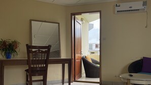 Ein Zimmer mit Holzschreibtisch, einem Stuhl, einem Spiegel, einem Korbstuhl und einem kleinen Tisch mit Fernbedienung.