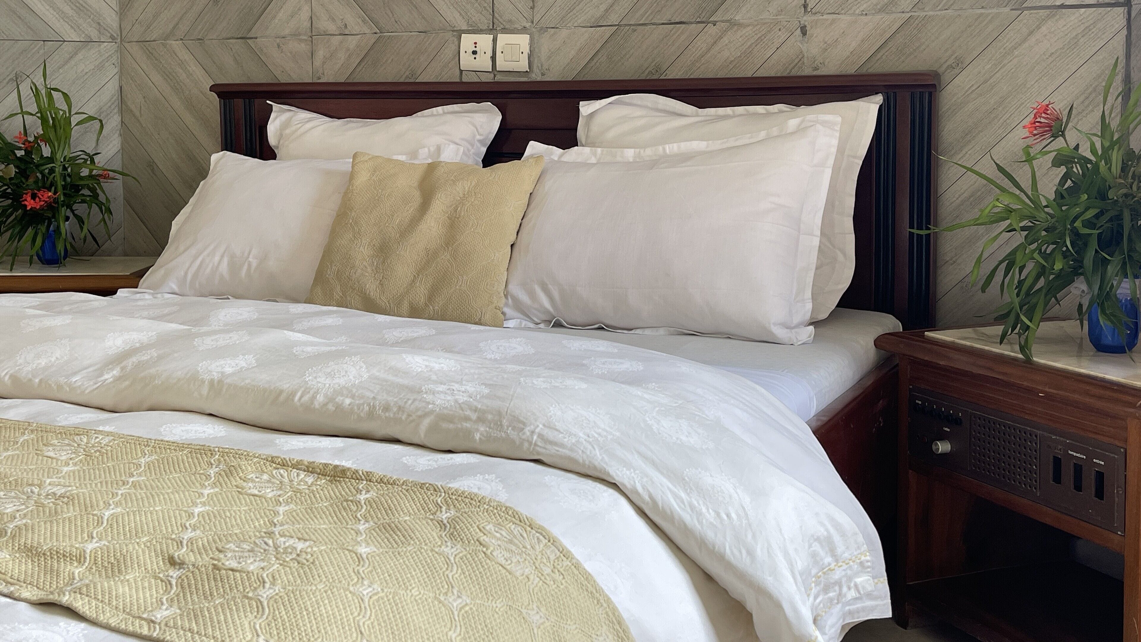 A neatly made bed with white linens and a beige throw blanket, wooden headboard, and bedside tables with lamps.