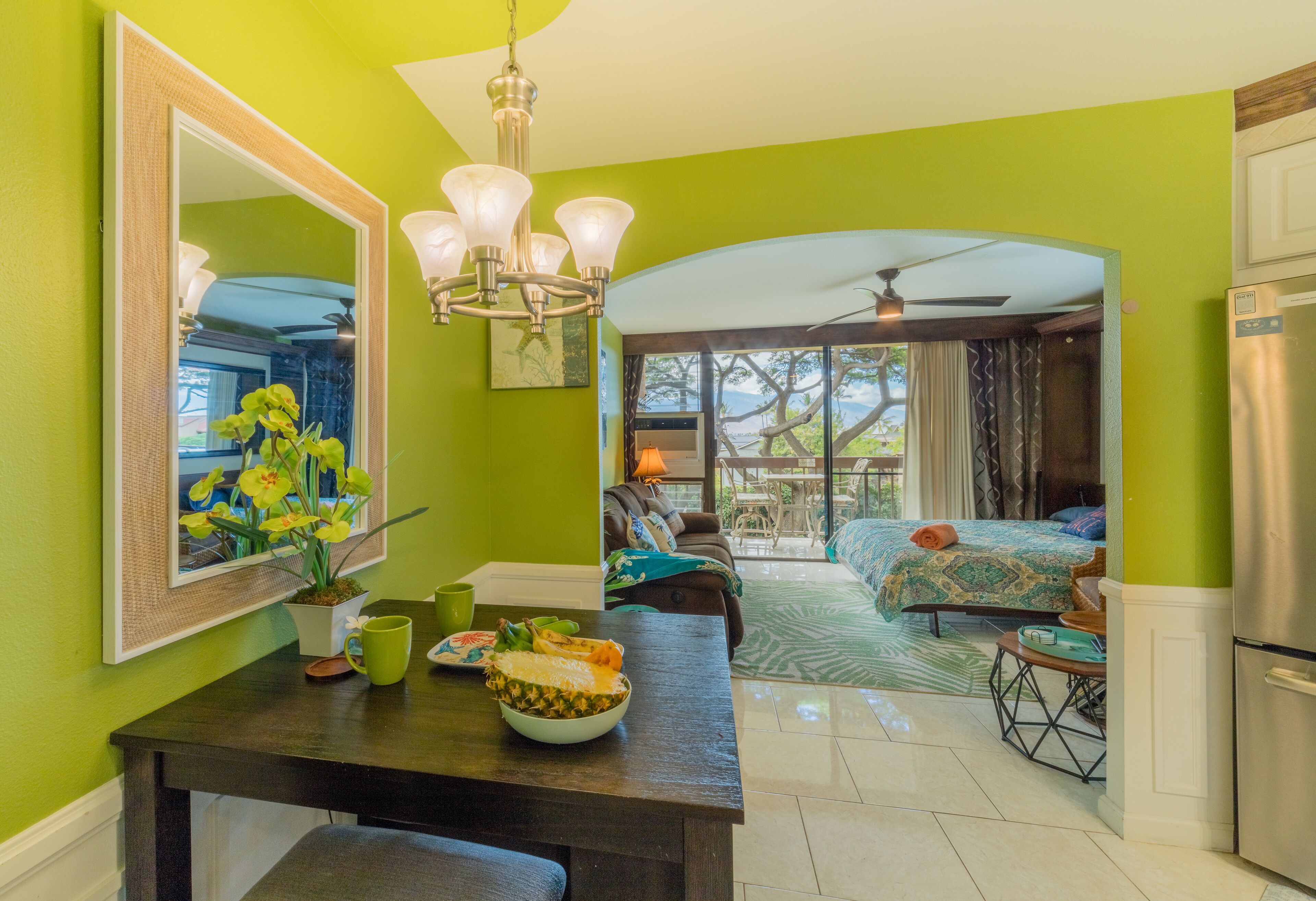 A bright green room with a dining area, a large mirror, and a view of the outdoors.