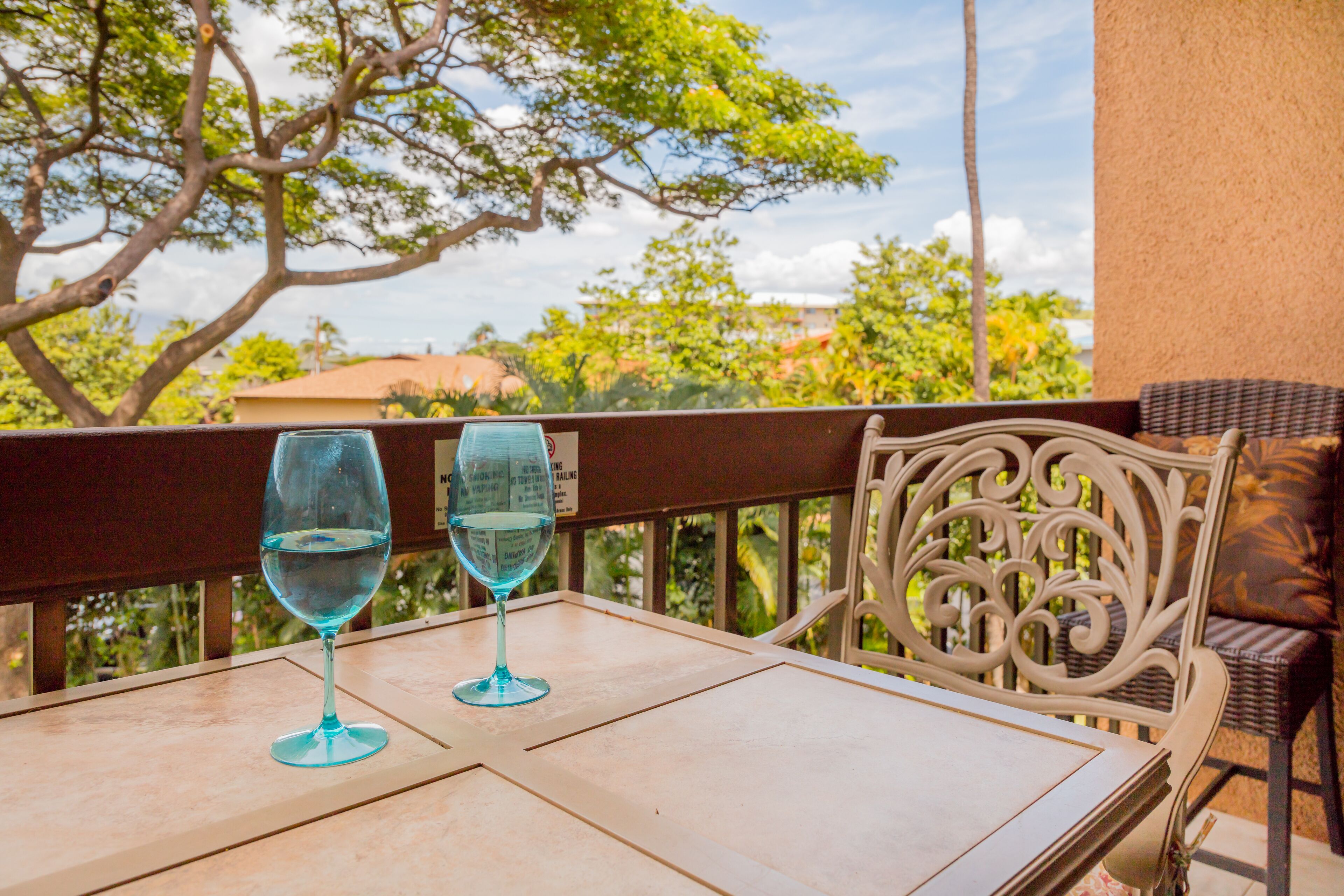 Una mesa con dos copas de vino blanco en un balcón con vistas a árboles y edificios.