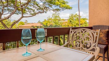 Una mesa con dos copas de vino blanco en un balcón con vistas a árboles y edificios.