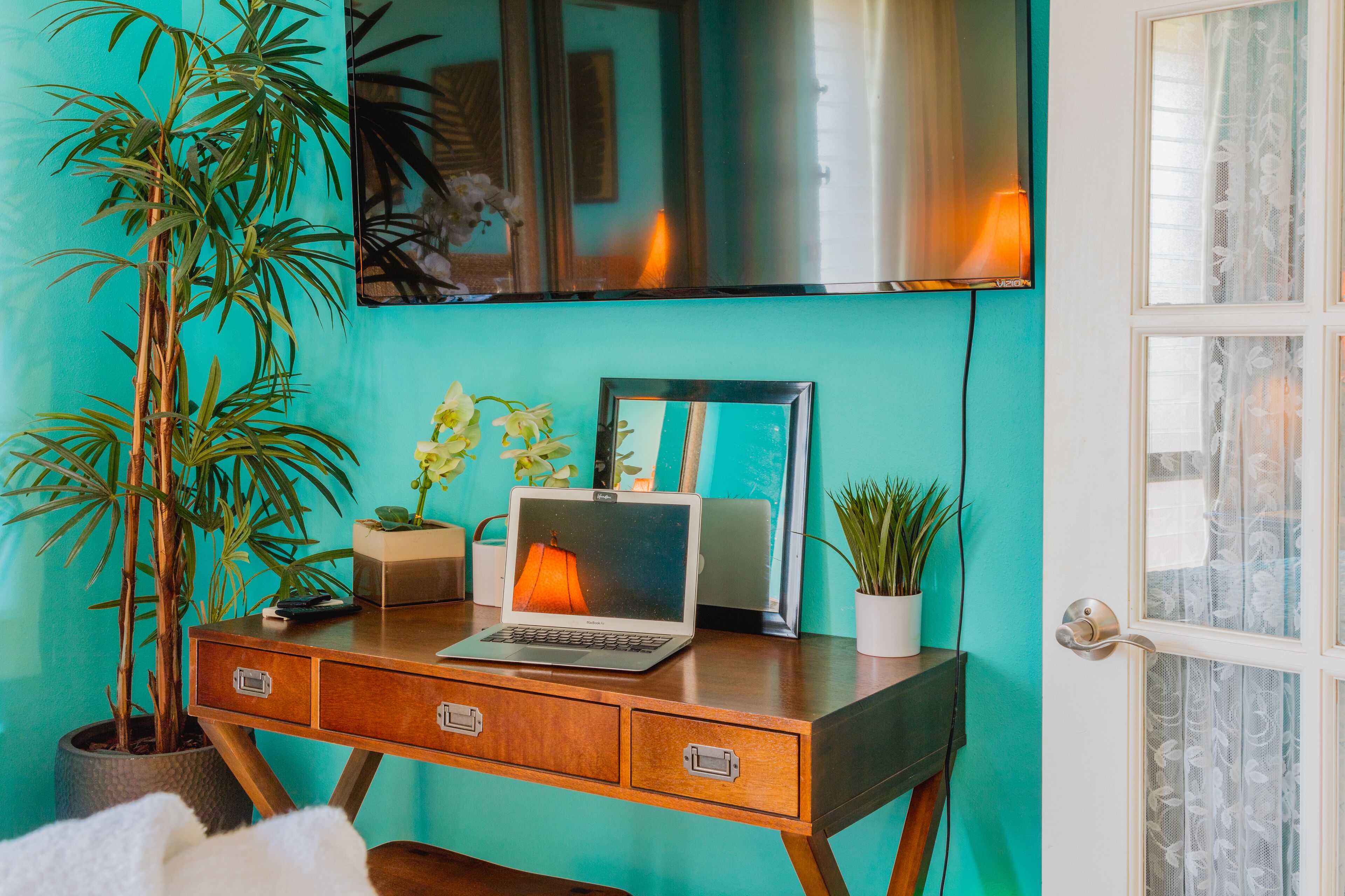 Pared de cor turquesa com uma mesa de madeira, um laptop, uma planta em vaso e um quadro emoldurado.