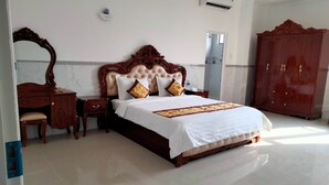 A spacious hotel room with a large bed, a wooden wardrobe, a desk with a chair, and a mirror on the wall. - Cao Lanh Hotel (My Tho)