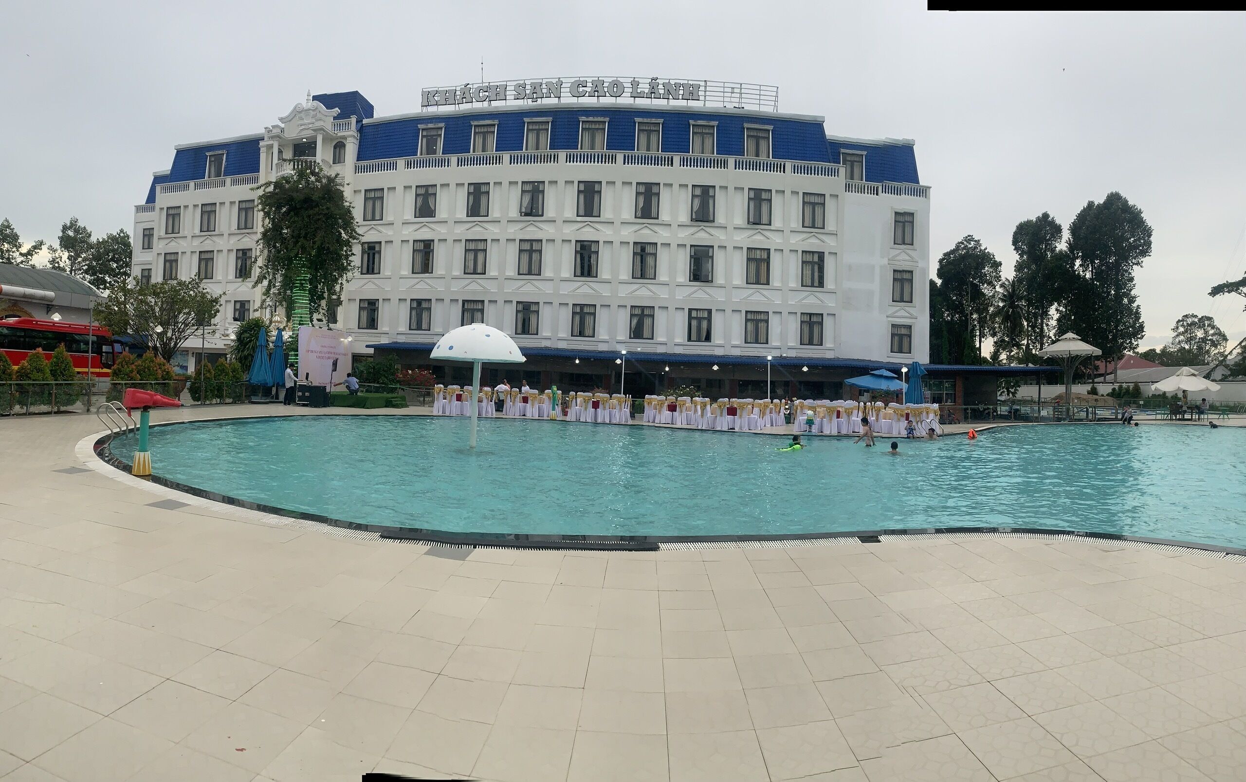 A hotel with a swimming pool, a stage, and a large building with a blue and white facade.