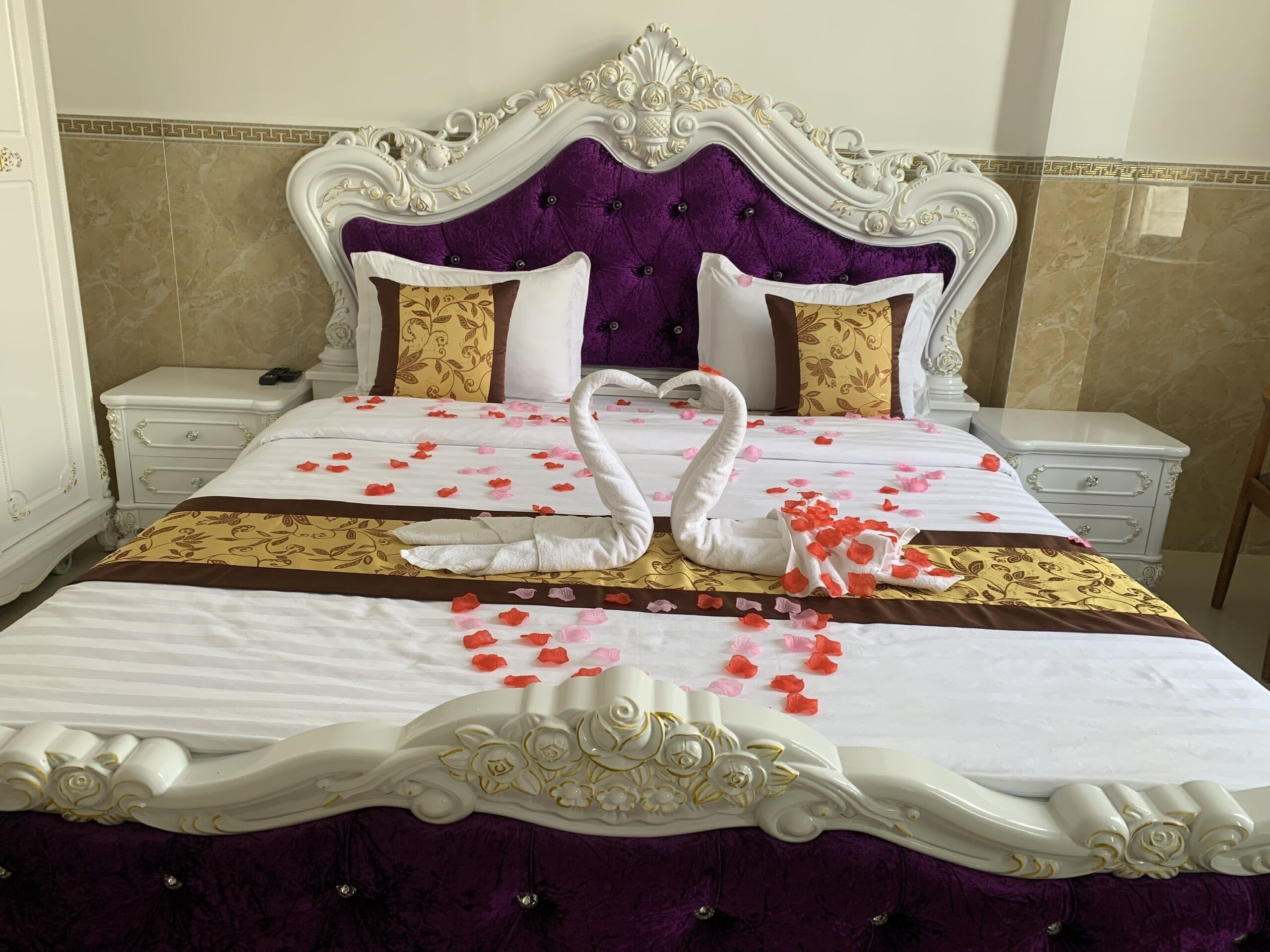 A bed with a purple headboard, white bedding, and decorative swan pillows.