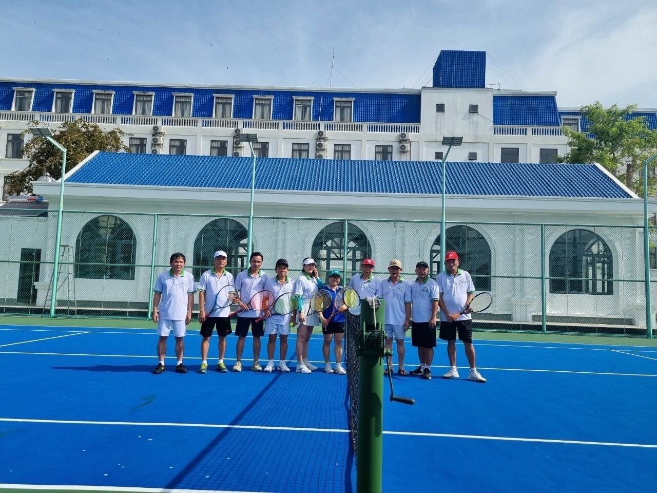 A group of people on a tennis court with a building in the background.
