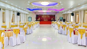 A banquet hall with rows of tables and chairs, a stage with a banner, and a chandelier. - Cao Lanh Hotel (My Tho)