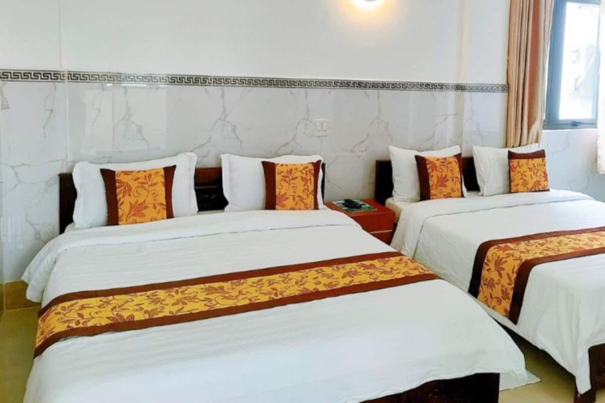 Une chambre d’hôtel avec deux lits, chacun agrémenté de draps blancs et de bordures décoratives marron. Une table de chevet en bois se trouve entre les lits, et une armoire rouge est placée à droite.