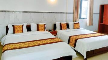 A hotel room with two beds, each with white linens and brown decorative borders. There is a wooden nightstand between the beds, and a red cabinet to the right.