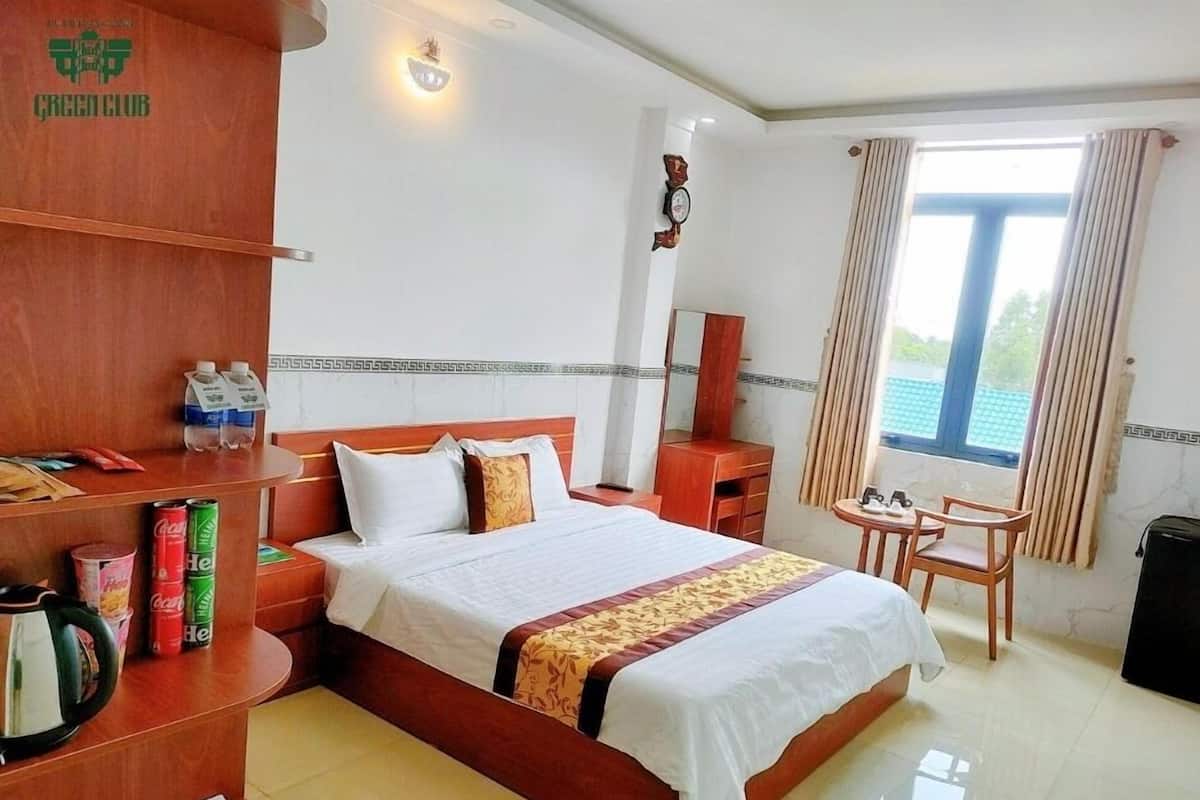 Une chambre d’hôtel comprenant un lit, des tables de chevet, une petite table ronde avec des chaises, un miroir et une fenêtre avec des rideaux.
