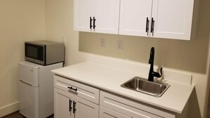 A compact kitchen with white cabinets, a stainless steel sink, and a microwave. - Private Guest Suite (Visalia)