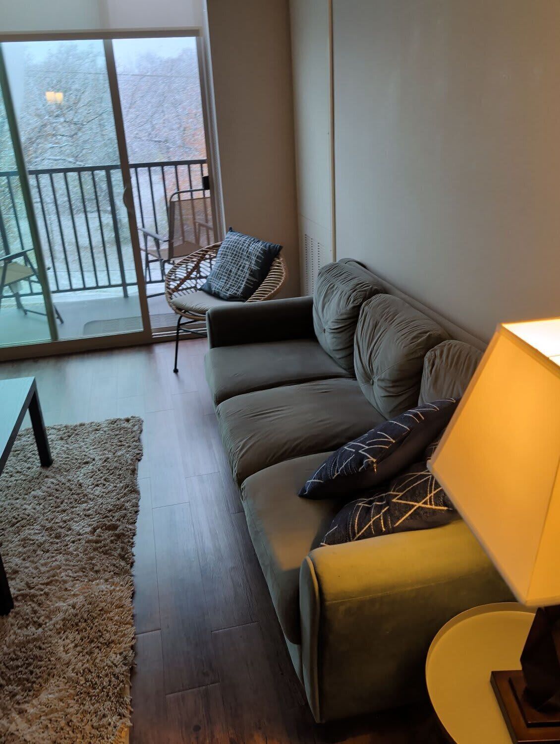 A modern living room with a grey sofa, a small round table, and a chair. There is a large window with a view of a snowy outdoor area.