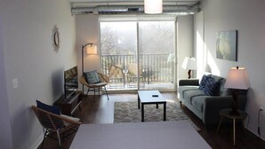 Ein geräumiges Wohnzimmer mit einem großen Schiebeglasfenster zum Balkon, einem Sofa, einem Couchtisch und einem Fernseher.